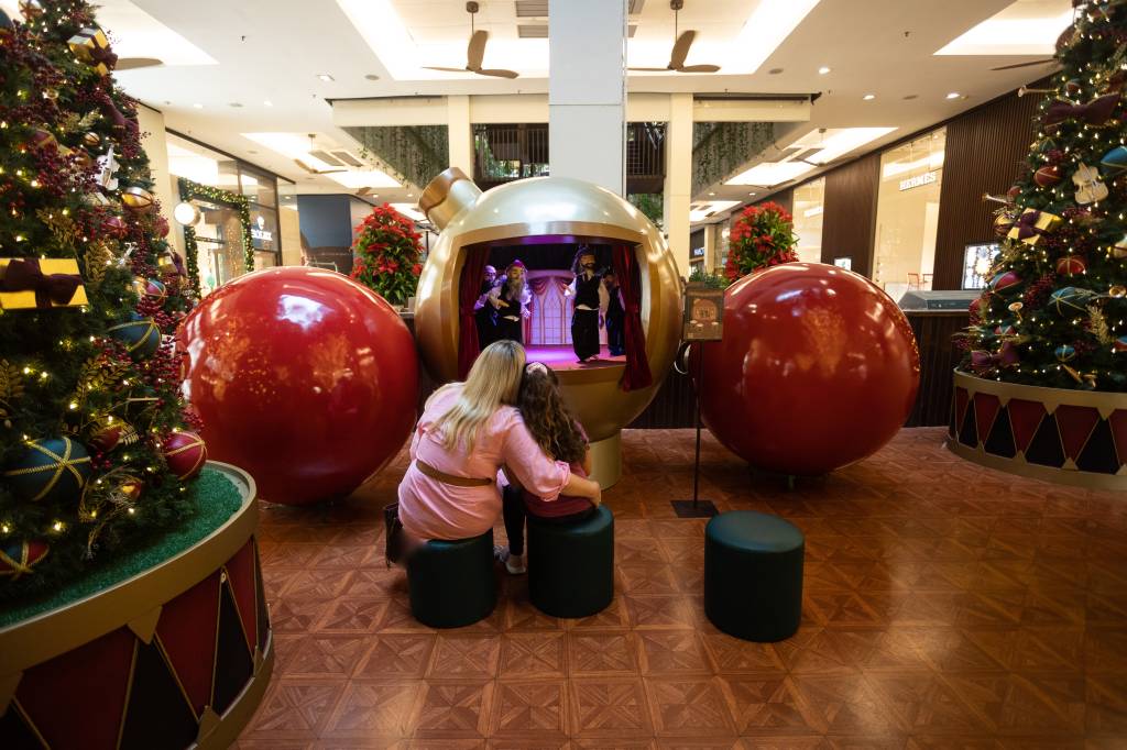 São Paulo, SP 19/12/2022 – NATAL – Shopping Cidade Jardim. Foto: Leo Martins Imagem mostra mãe loira e criança de costas, sentadas e abraçadas, assistindo a mini-teatro de fantoches em espaço com chão de madeira e duas bolas gigantes vermelhas nas laterais.