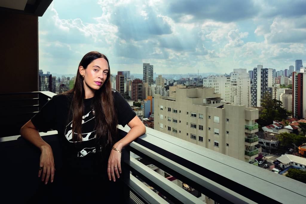 Francesca Alterio Imagem mostra mulher de roupa preta apoiada em sacada de varanda, com horizonte de prédios ao fundo