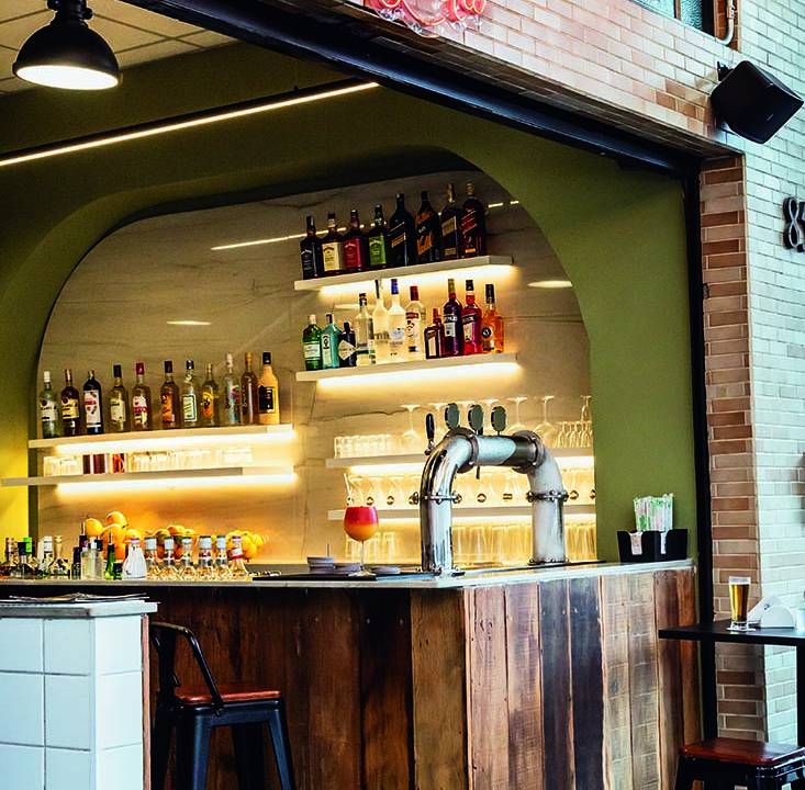 Ambiente balcão de madeira e bar ao fundo com bancos altos
