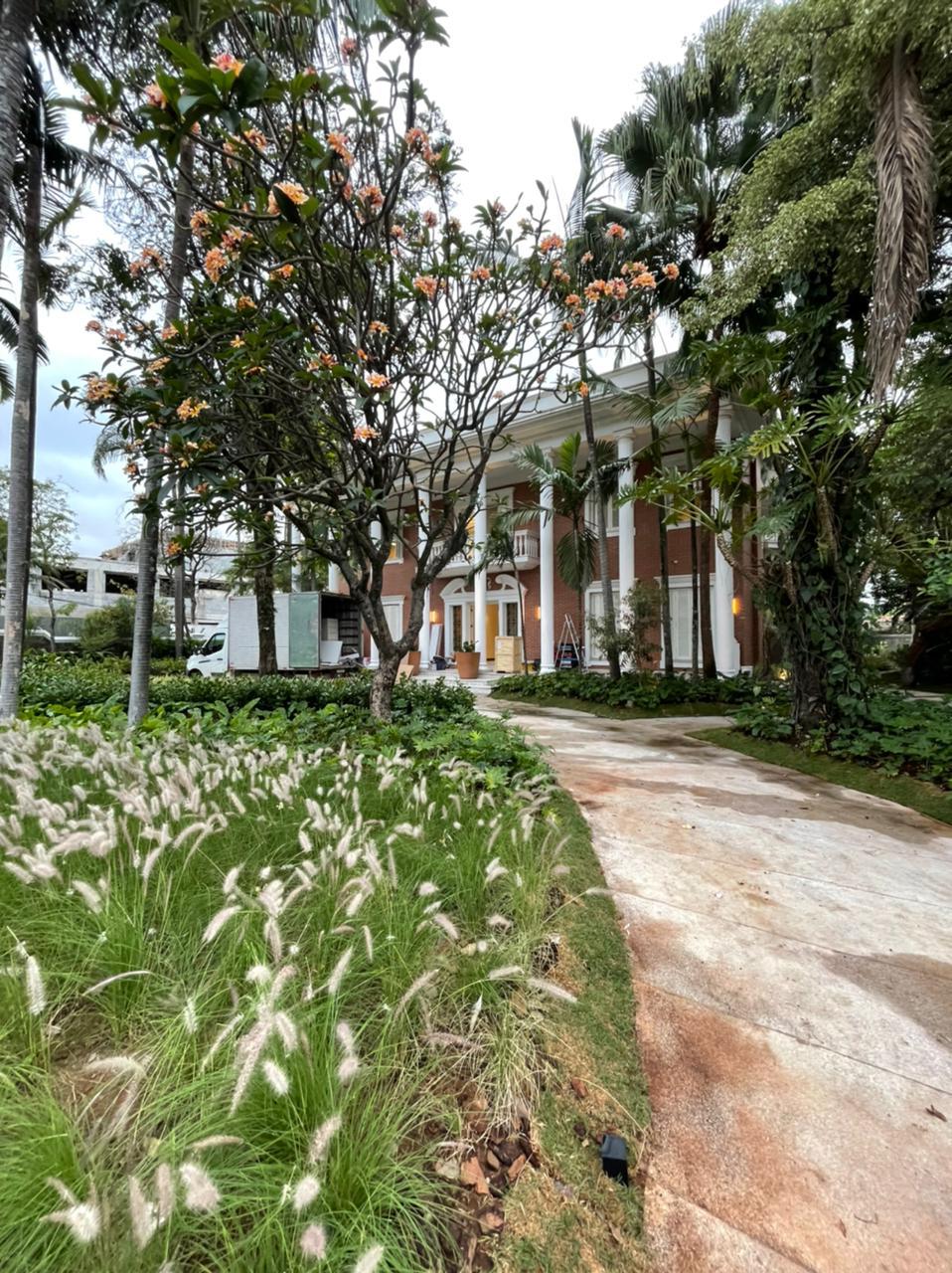 Núcleo GA – Jardins (Arquivo Pessoal) (2) Jardim com plantinhas brancas, passarela de concreto e árvores ao fundo escondem mansão de dois andares.
