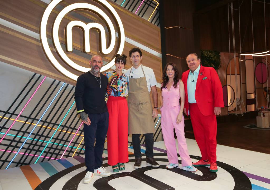MasterChef Brasil Cinco pessoas, sendo três homens com uma mulher entre eles, e o símbolo do MasterChef atrpas