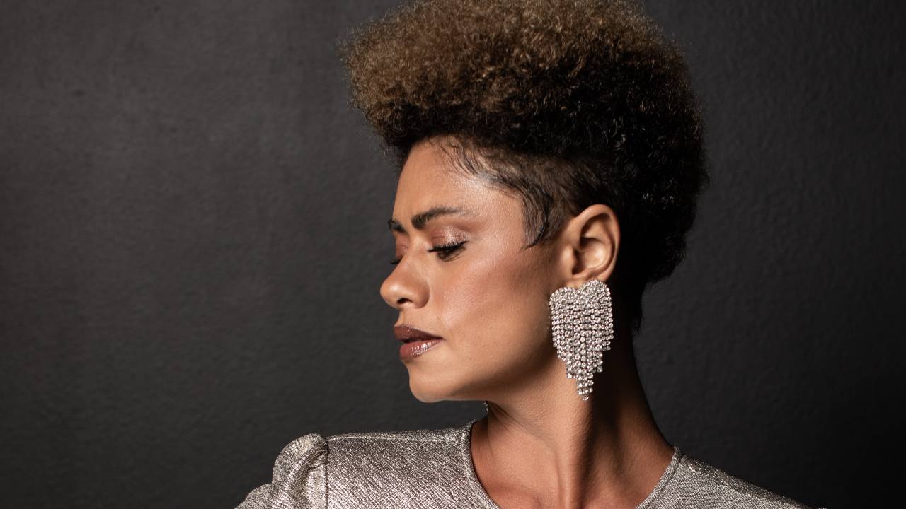 Mulher negra posa olhando para o lado com mão na cintura e vestido prata.