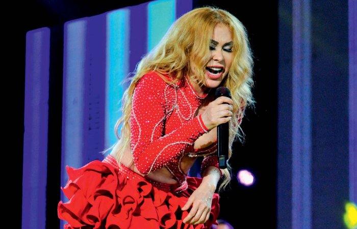 Imagem mostra mulher de vestido vermelho cantando em microfone