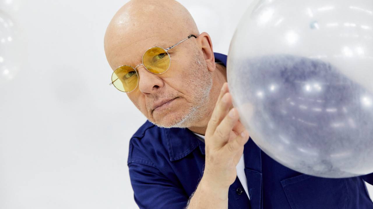 Homem branco careca aparece atrás de bola transparente.