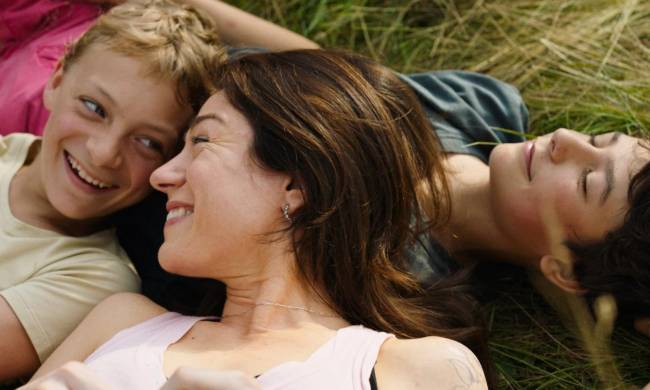 Close filme Mulher sorri no meio de dois meninos enquanto estão deitados na grama