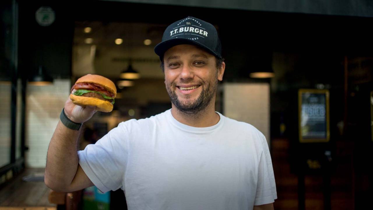 homem de branco com boné preto segura hamburguer