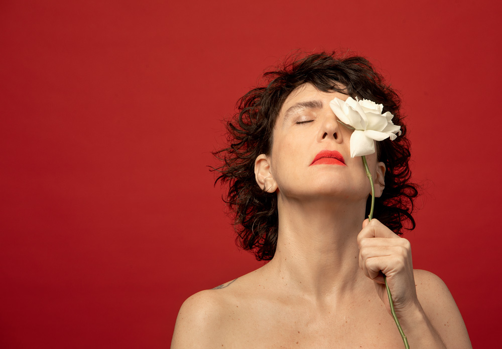 Imagem mostra mulher segurando flor sobre fundo vermelho