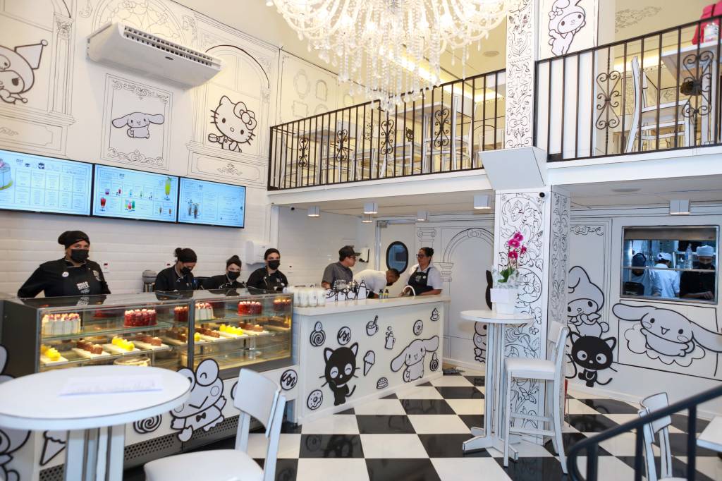 Café Hello Kitty Ambiente de cafeteria da Hello Kitty com chão quadriculado preto e branco, paredes brancas com desenhos em preto e balcão de doces com atendentes à esquerda.