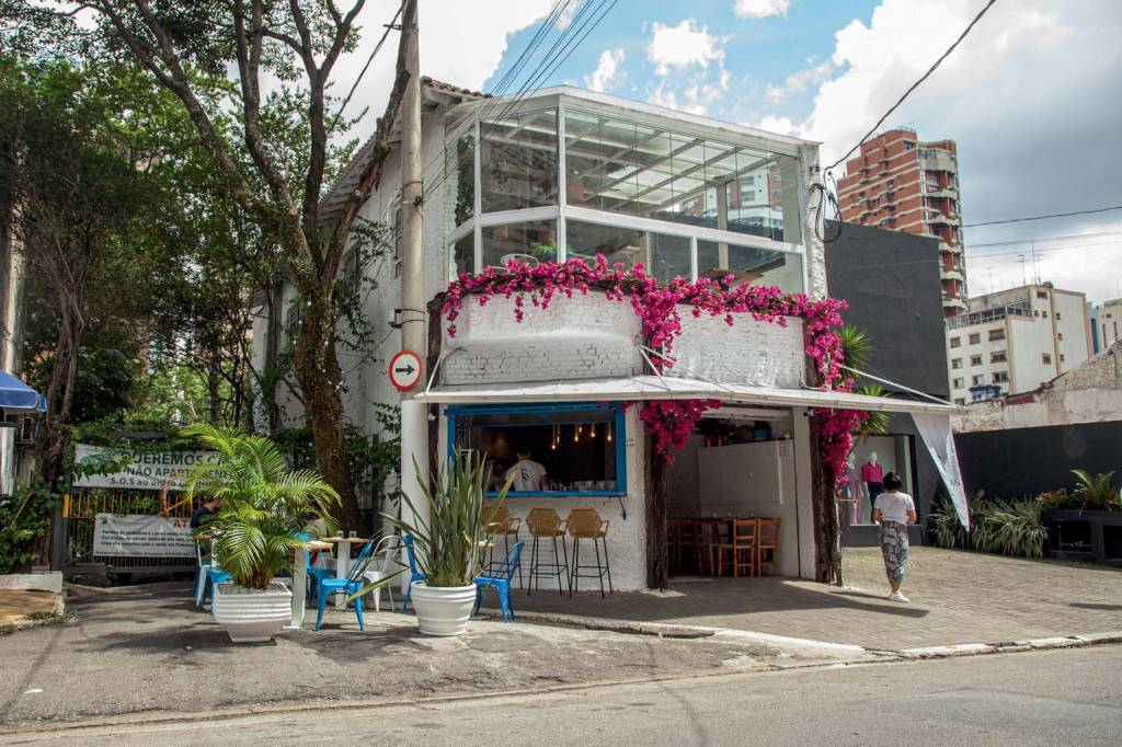 Petros Greek Taverna Fachada do restaurante Petros Greek Taverna, sobrado branco com segundo andar de vidro, banquetas na frente e flores primavera trepadas na parede.