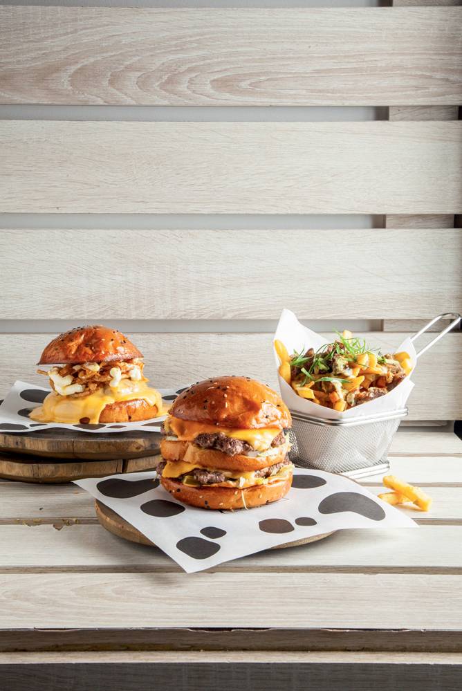 Fat Cow Dois hambúrgueres ao lado de porção de fritas em cestinha de metal.