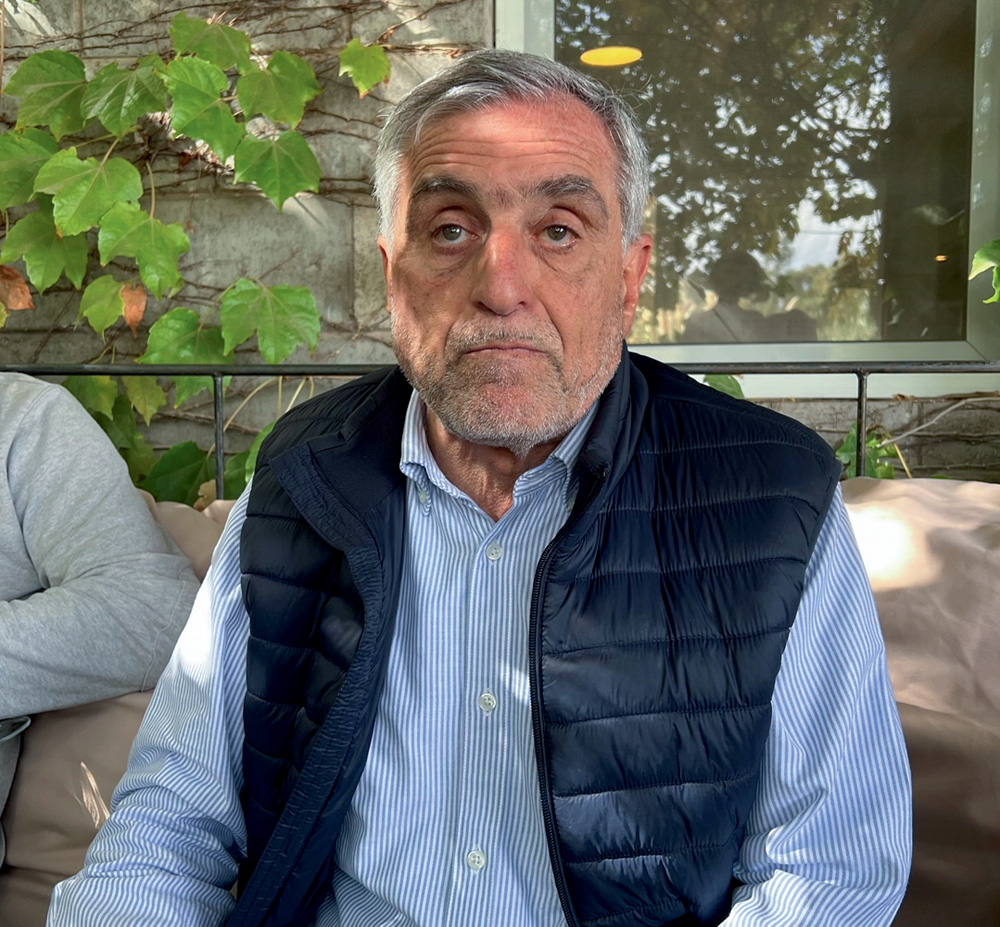 Homem branco de camisa social azul e colete puffer.