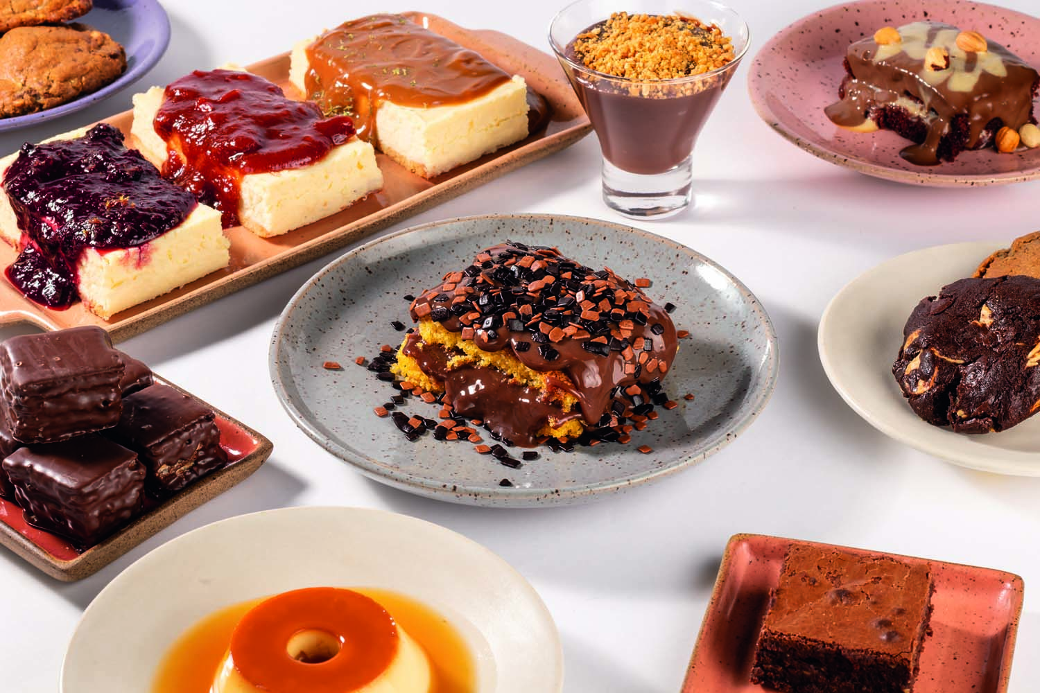 Diferentes tipos de sobremesa (bolo de cenoura, cheesecake, pudim, mousse) sobre superf&iacute;cie branca.