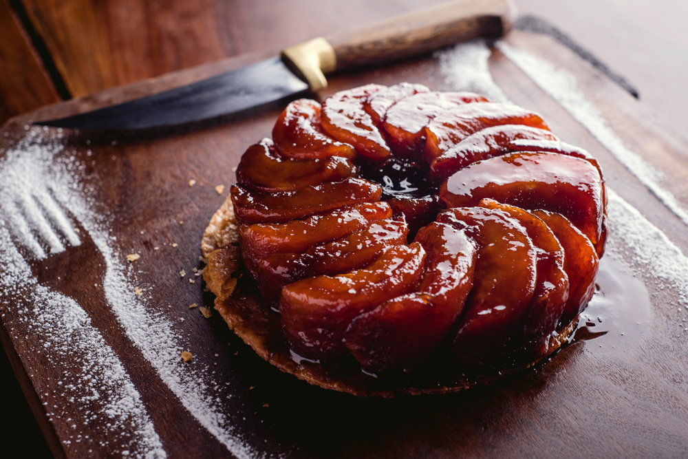 Tarte tatin com gomos caramelados de ma&ccedil;&atilde; sobre tampo de madeira.