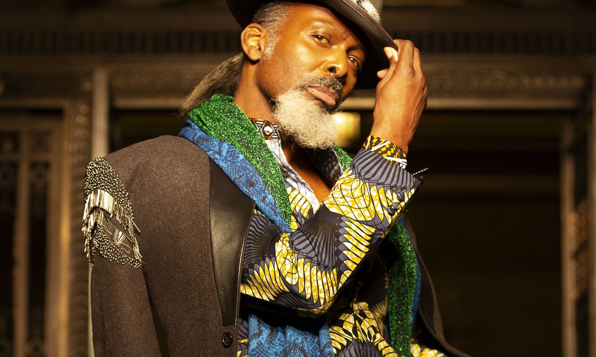 um homem negro de chapéu, camisa estampada e terno