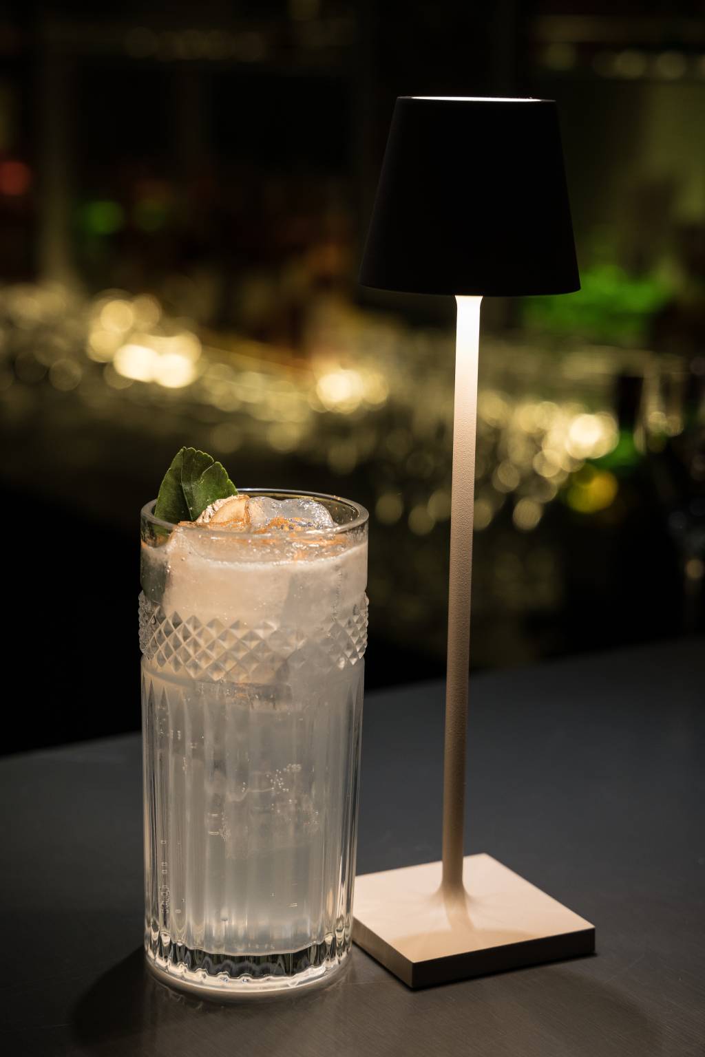 Speakeasy Casacor Copo longo de drinque ao lado de mini abajour.