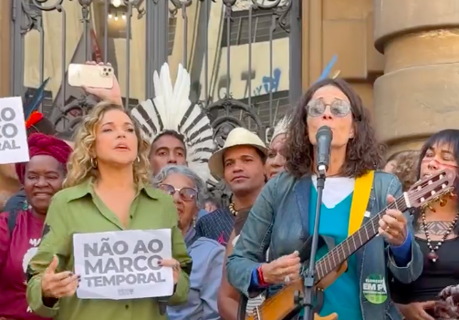 daniela mercury segurando um papel escrito "não ao marco temporal" e zélia duncan com seu violão cantando ao microfone