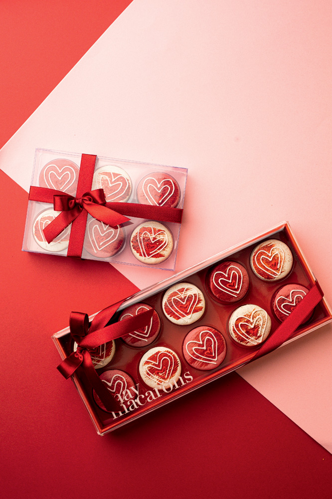 Dia dos Namorados – May Macarons Duas caixas de macarons sobre superfície rosa claro e vermelho.
