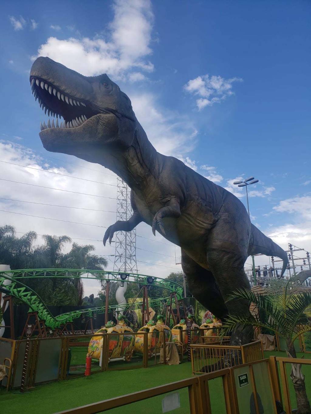 T-Rex Park Maquete de tiranossauro rex ao lado de montanha-russa.