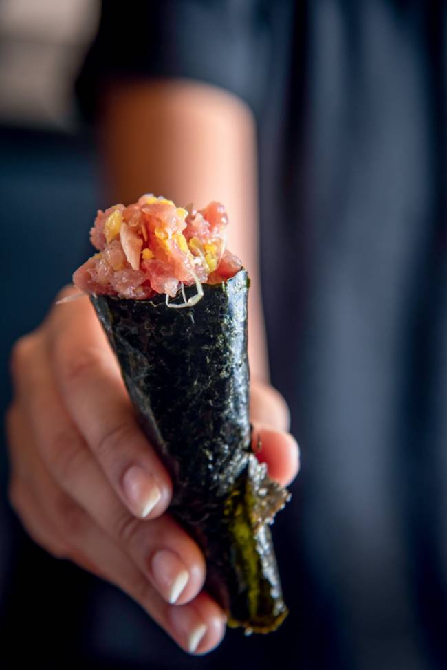 Mãos segurando mini temaki de peixe.