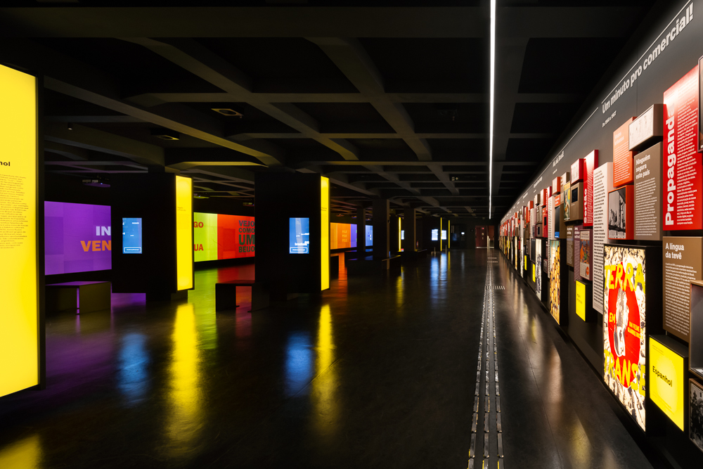 um galpão escuro com luzes coloridas e uma parede com obras iluminadas