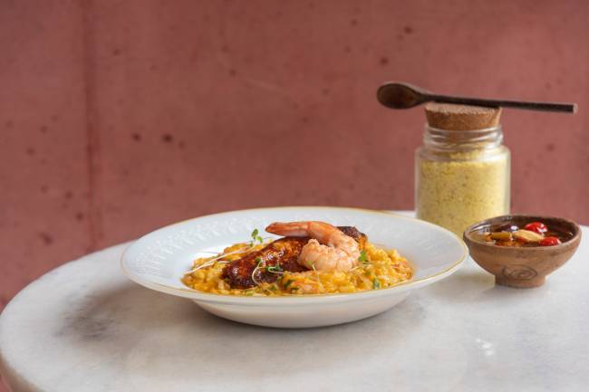 Aconchegante Bar Prato de louça branca com arroz coberto por camarão em mesa de tampo branco.