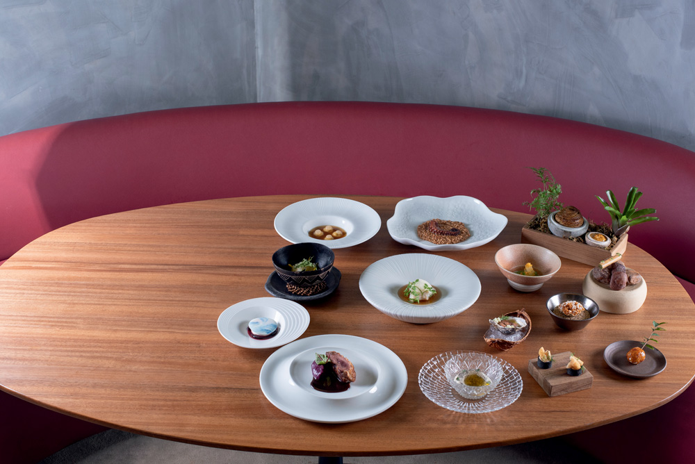 COMER & BEBER 2023 – Notiê – Priceless Mesa de madeira em formato oval com diversos pratos e cumbucas com comidas.