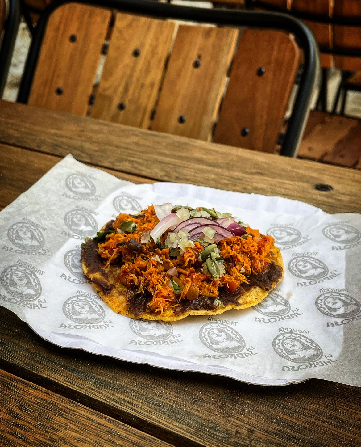 Taco aberto sobre prato de papel em mesa de madeira.