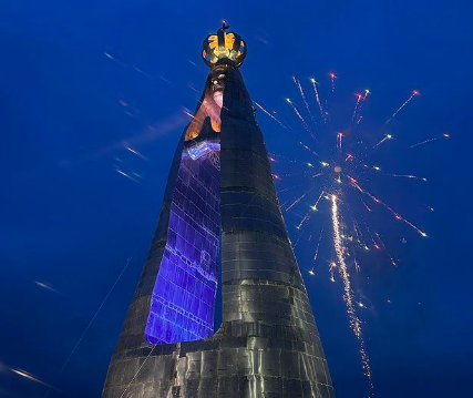 imagem mostra grande estátua de Nossa Senhora, com vão no meio e fogos de artifício no céu no momento da foto