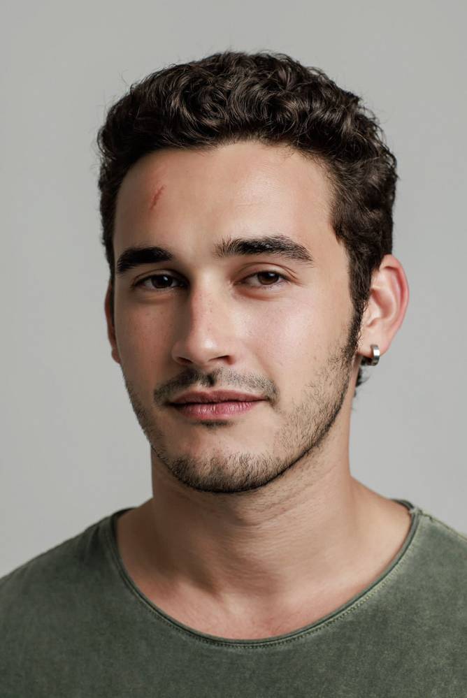 Filipe Bragança (Jorge Bispo-Divulgação).jpeg (1) Jovem branco de barba rala e cabelo espesso escuro encara a câmera com meio sorriso. Um pequeno machucado avermelhado aparece discretamente na testa.