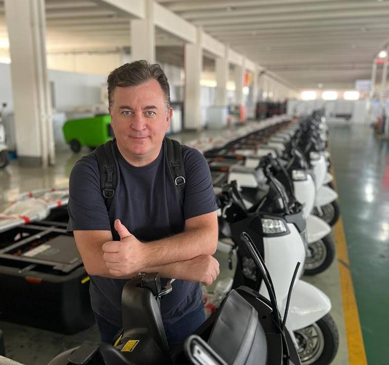 Homem branco posa apoiado em fileira de triciclos.
