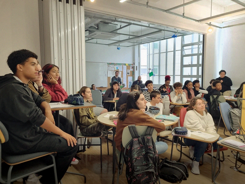 camino school Imagem mostra diversos alunos em sala de aula que tem mesas redondas e grande janela de vidro ao fundo