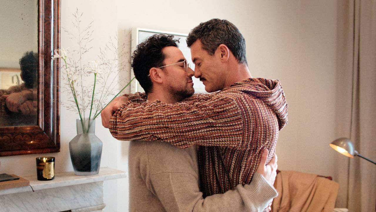 Casal de homens gays aparece abraçado dentro de sala de estar