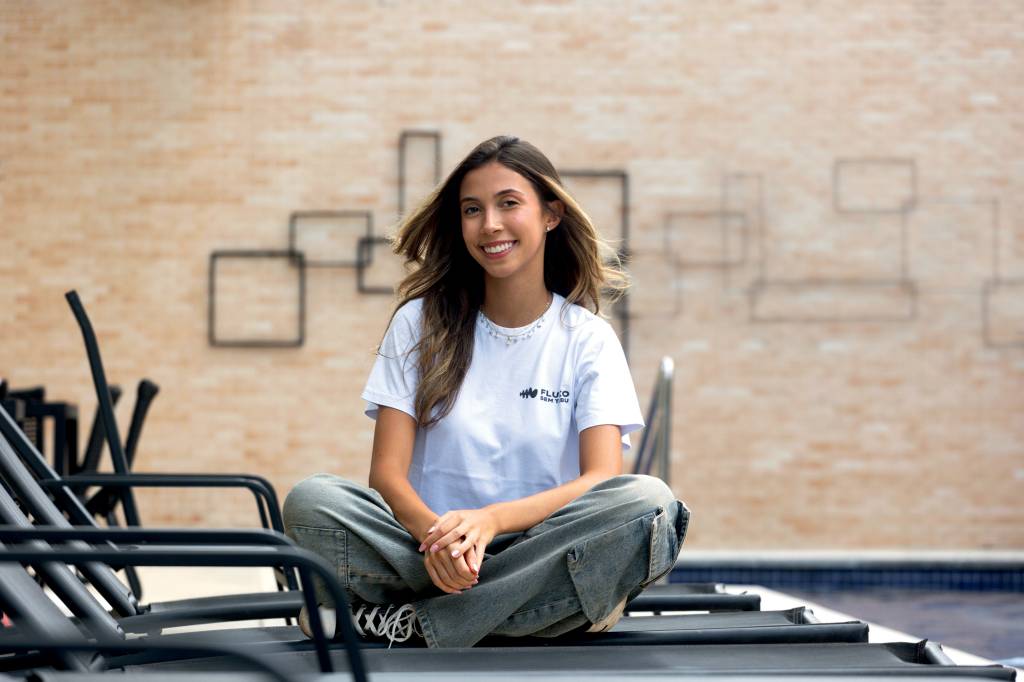 luana escamillo Imagem mostra Luana sentada em cadeira de piscina com pernas cruzadas, olhando para a foto sorrindo
