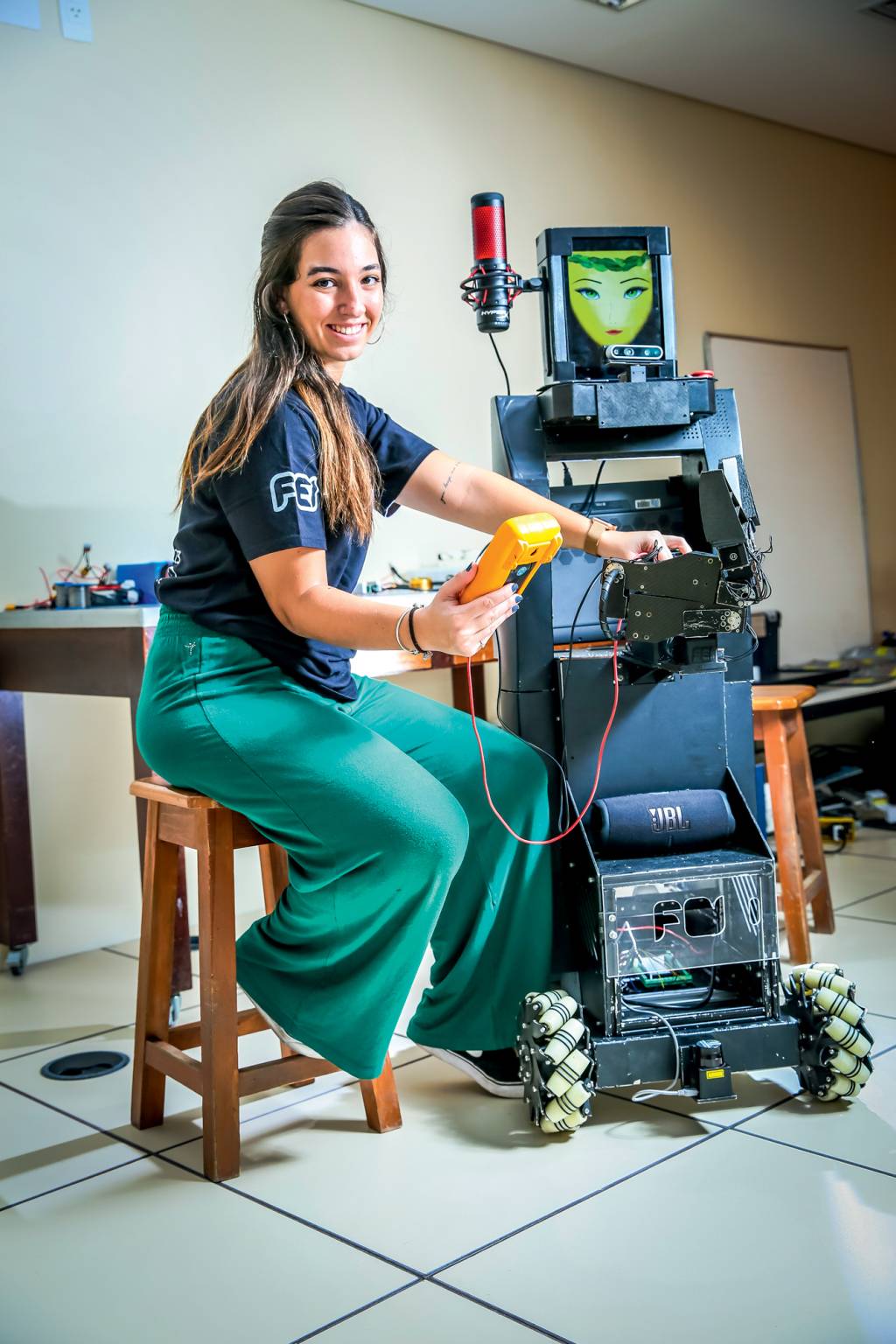 flora aidar Imagem mostra jovem sentada ao lado de robô que tem tela com rosto. Ela segura aparelho e sorri para a foto