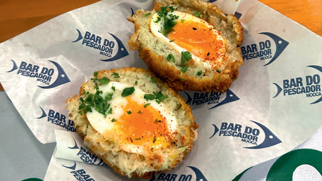 Bolovo de bacalhau cortado ao meio com a gema cremosa coberto por ervas frescas