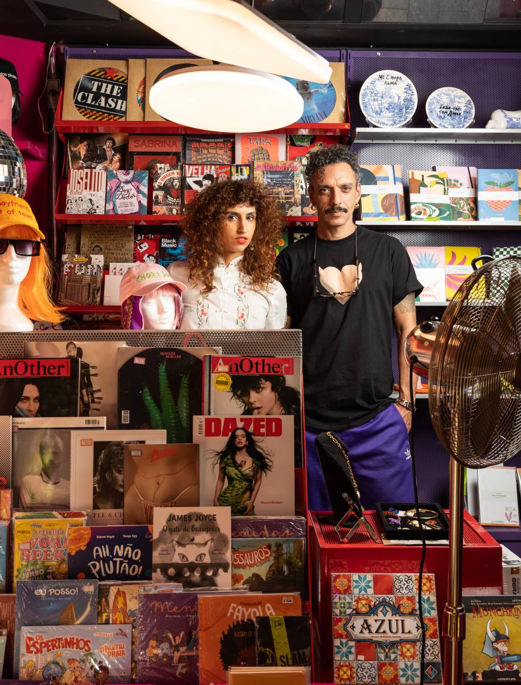 Botando Banca, Tatá Sausmikat e Ariel Bemergui Crédito Leo Martins-Veja SP (6) Casal posa atrás de prateleira cheia de revistas estrangeiras iluminadas por spot