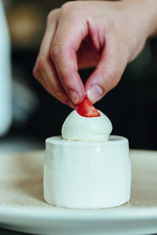 Mão colocando morango no entremet de morango e mascarpone