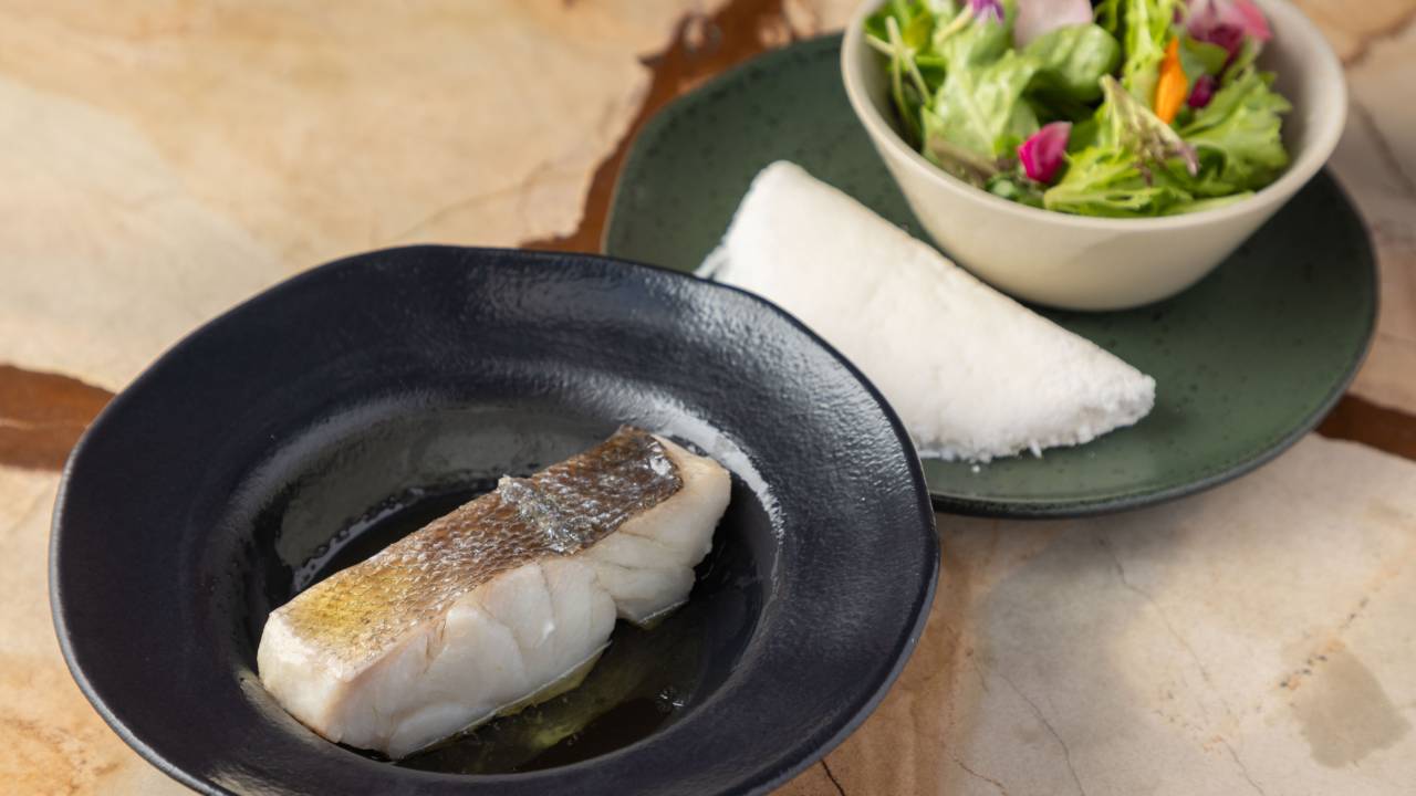 Prato de peixe no vapor em um caldo e prato com tapioca e hortaliças pancs