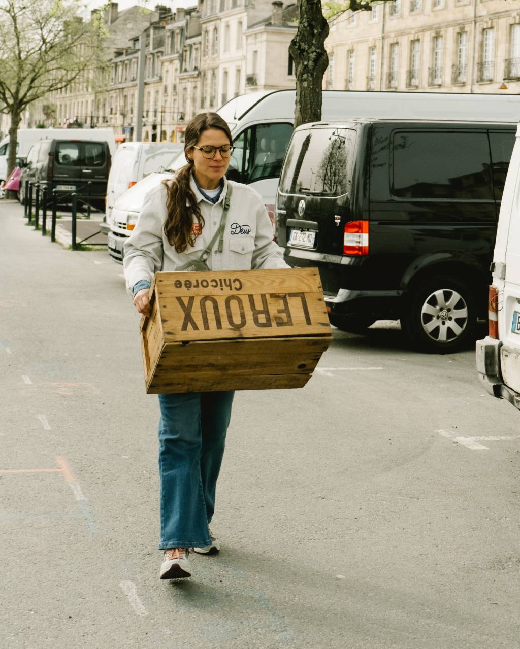 DSCF8226 Moça com rabo de cavalo carregando caixa em rua na França, com carros estacionados à direita