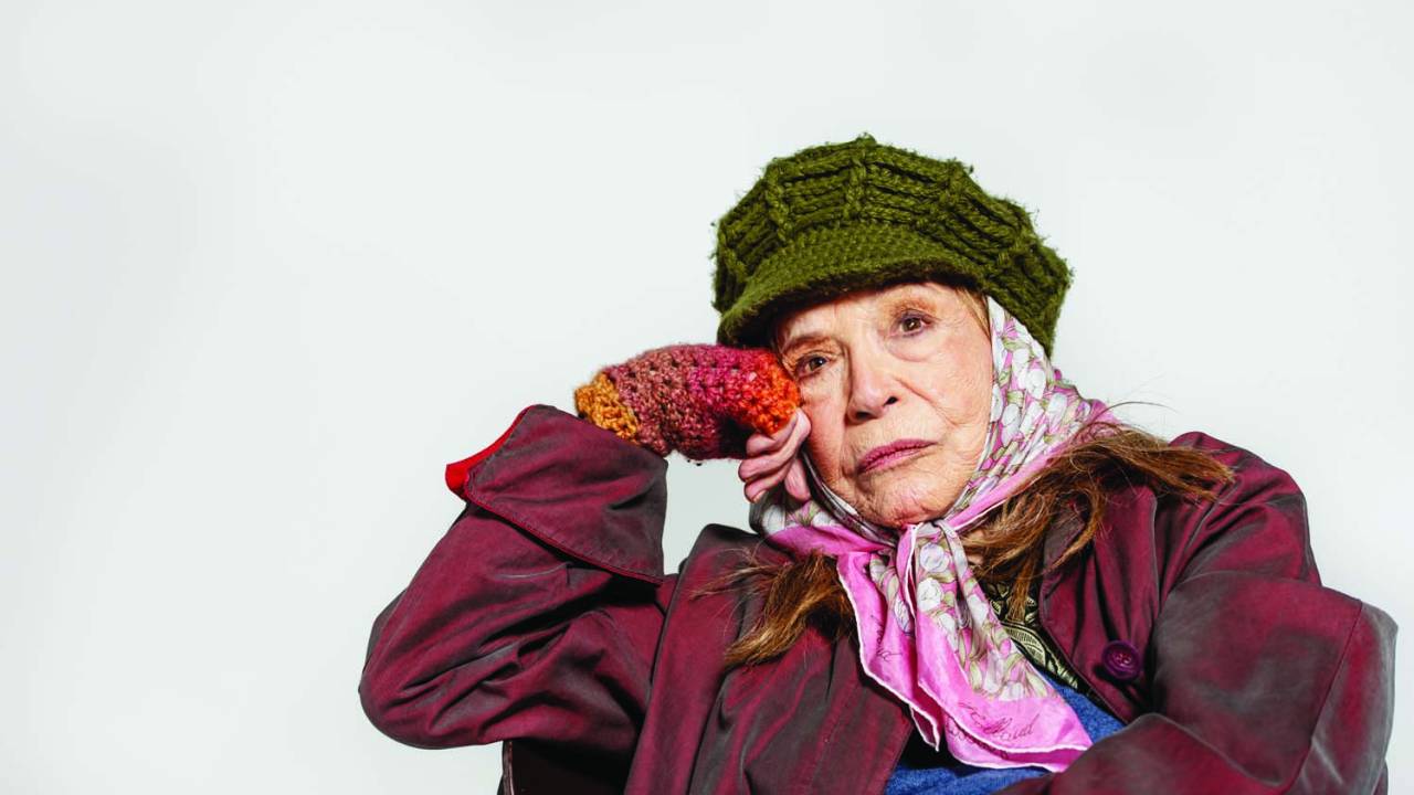Senhora com roupas coloridas e peças de crochê posa com mão no rosto