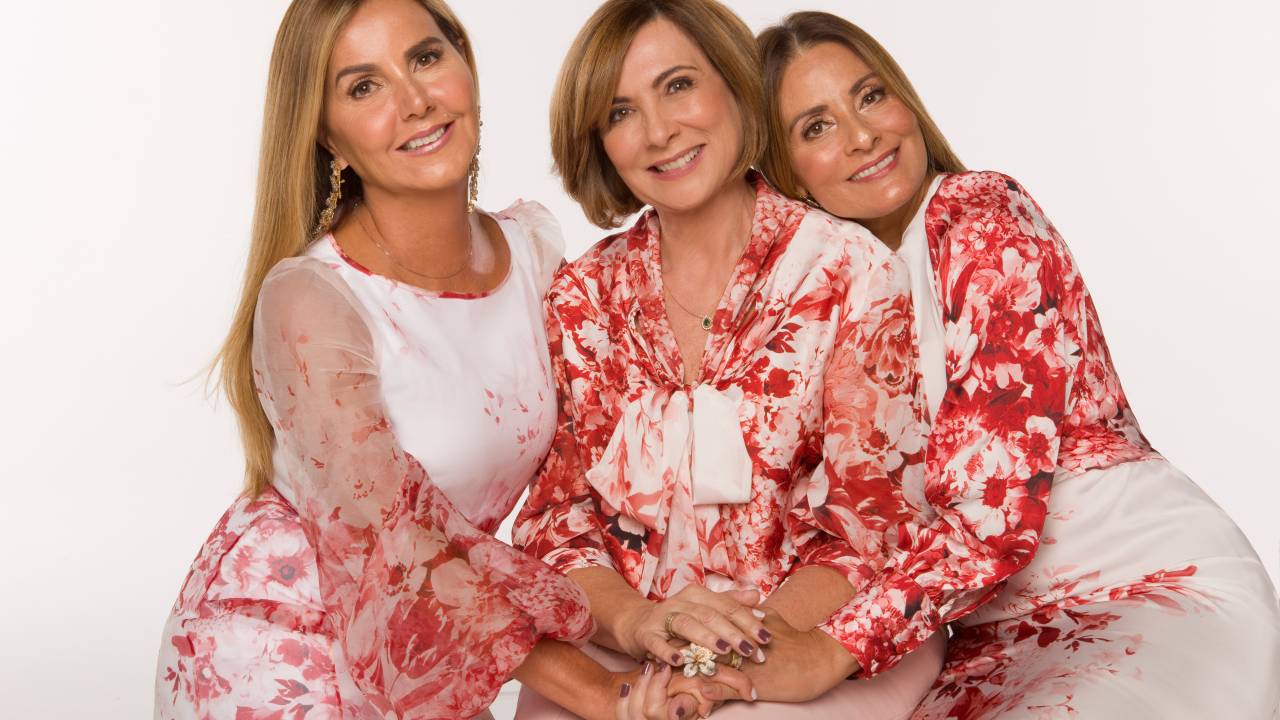 Três mulheres posam vestindo roupas brancas com estampas de rosas