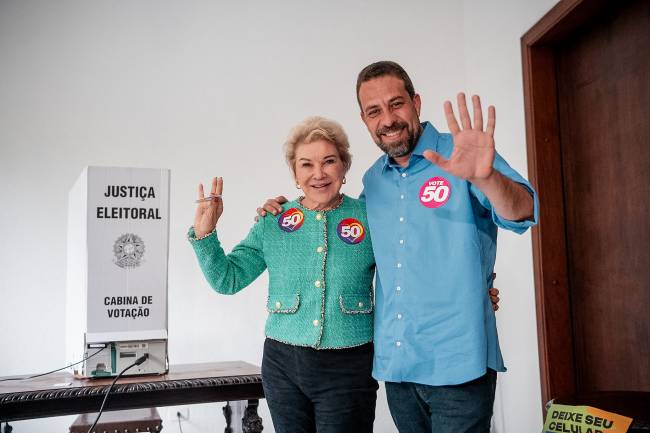 Duas pessoas sorrindo e fazendo gesto com as mãos formando 50