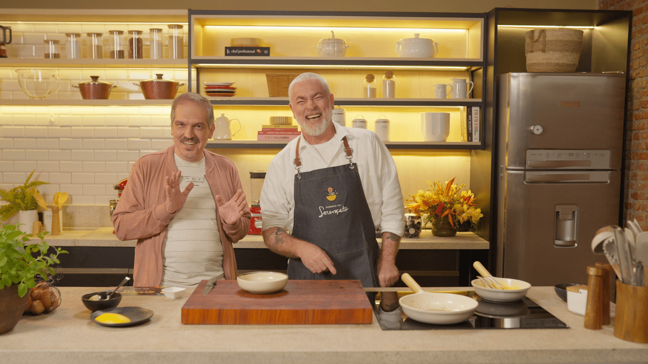 Atrás de um balcão de cozinha estão, dé é o jornalista Arnaldo Lorençato e o chef Alex Atala