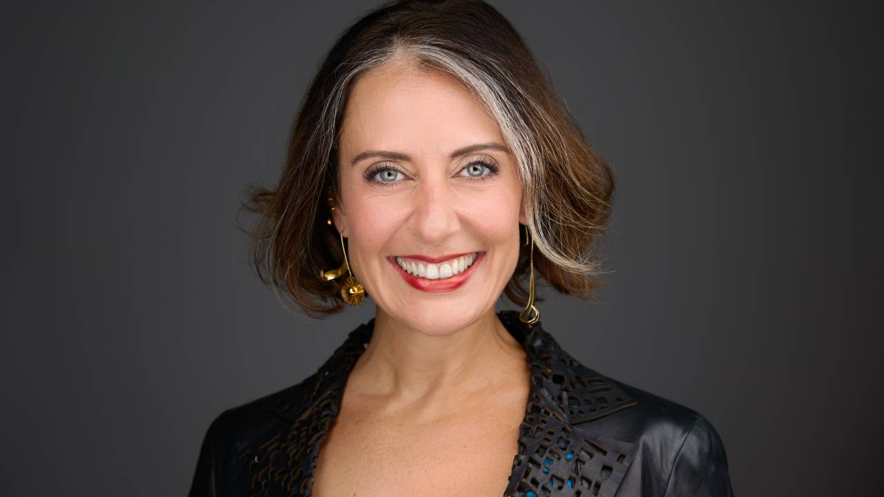 Mulher de cabelo loiro escuro sorri e veste blazer preto