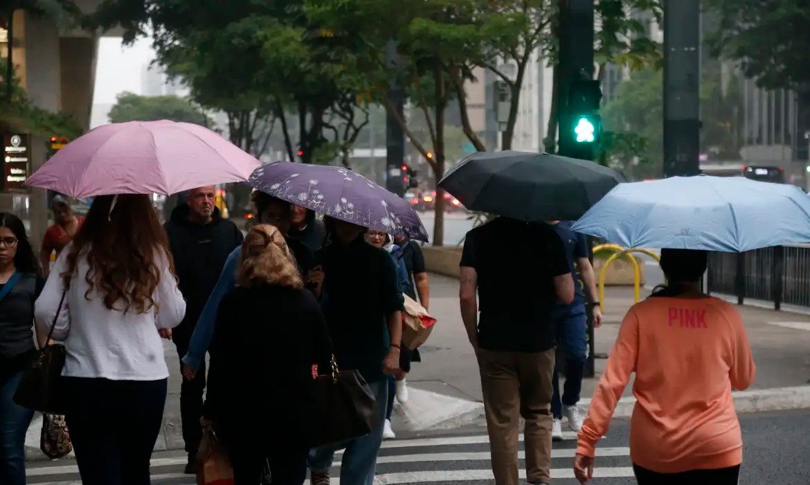 Pessoas segurando guarda-chuvas e andando na rua