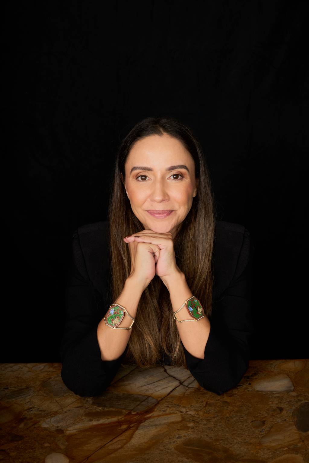 Ana Damous Crédito Luiza Ananias-Divulgação (2) Mulher branca de cabelos longos com mãos no queixo sentada em mesa com pulseiras à mostra