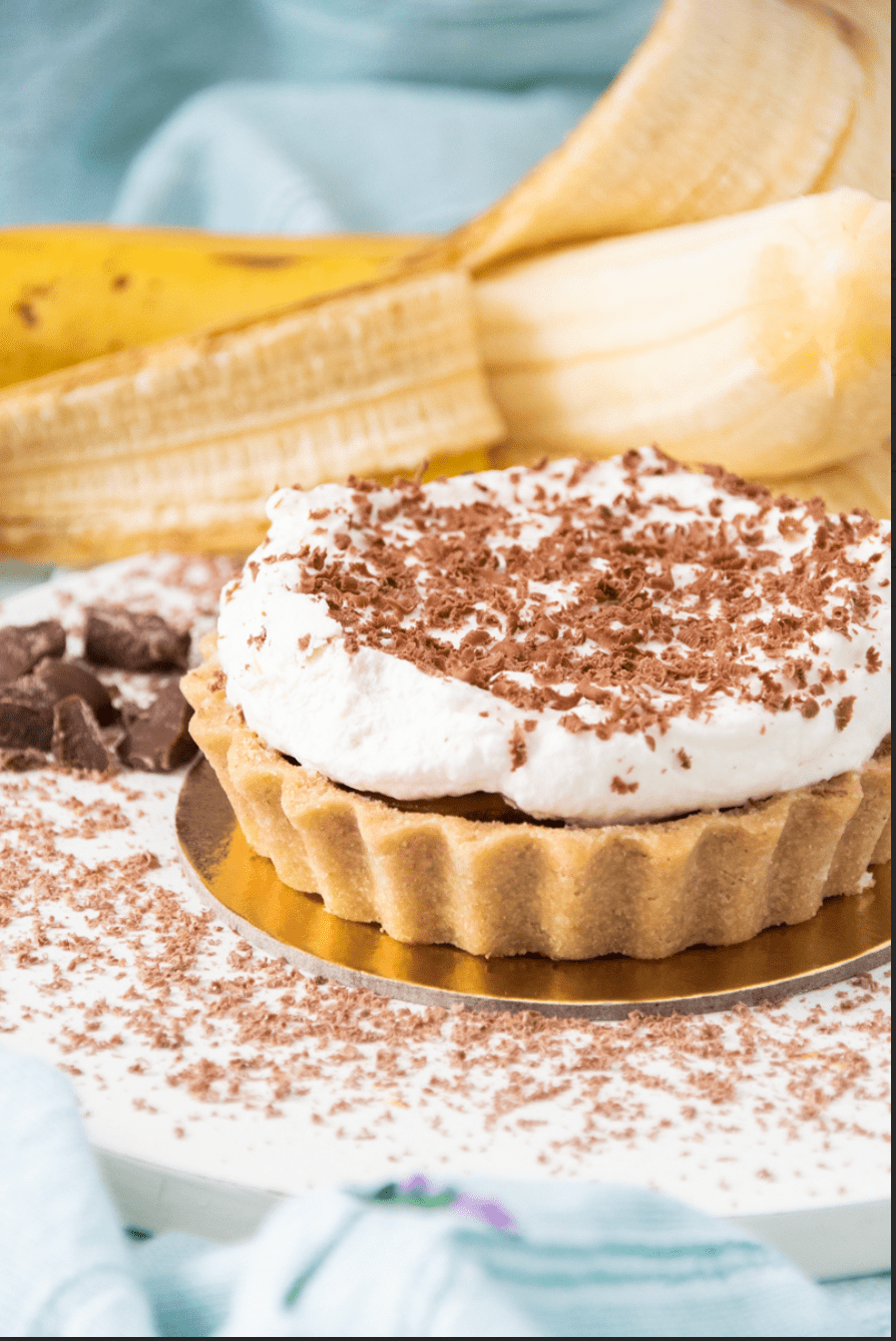 Canelle_Banoffee_Cred. Victoria Caldini (1) Torta em cima de recipiente dourado e banana atrás