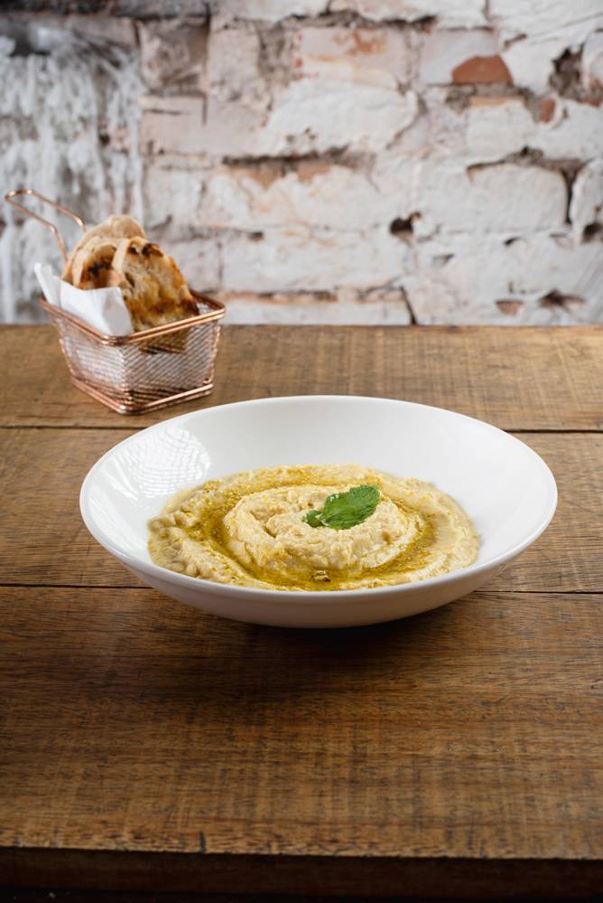 Balcone -Hommus com pistache 009.jpg Creme bege em cima de prato branco e mesa de madeira