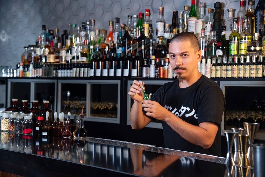 Tan Tan O head bartender do Tan Tan, Caio Carvalhaes, preparando um drink no balcão enquanto posa para a foto