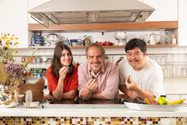 Três pessoas sorrindo e uma cozinha ao fundo